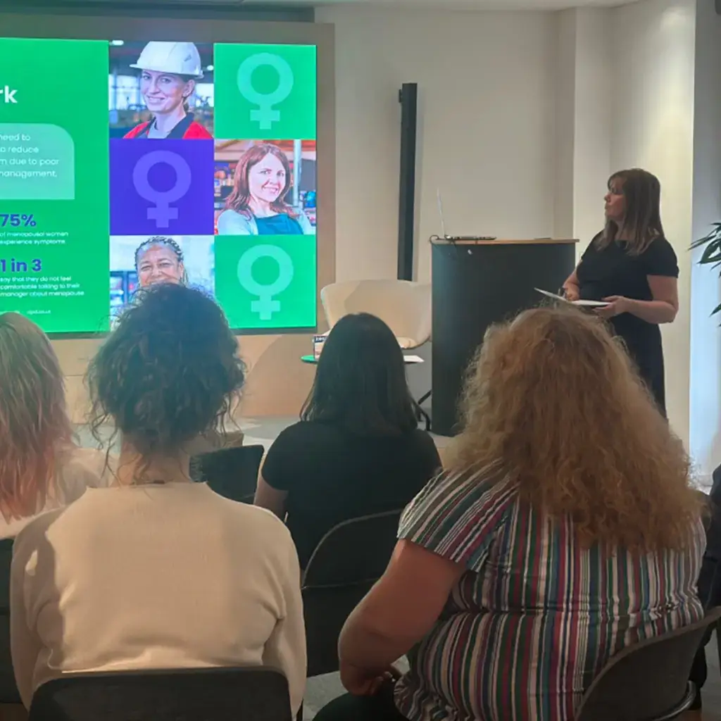 A woman giving a presentation to a seated female audience.