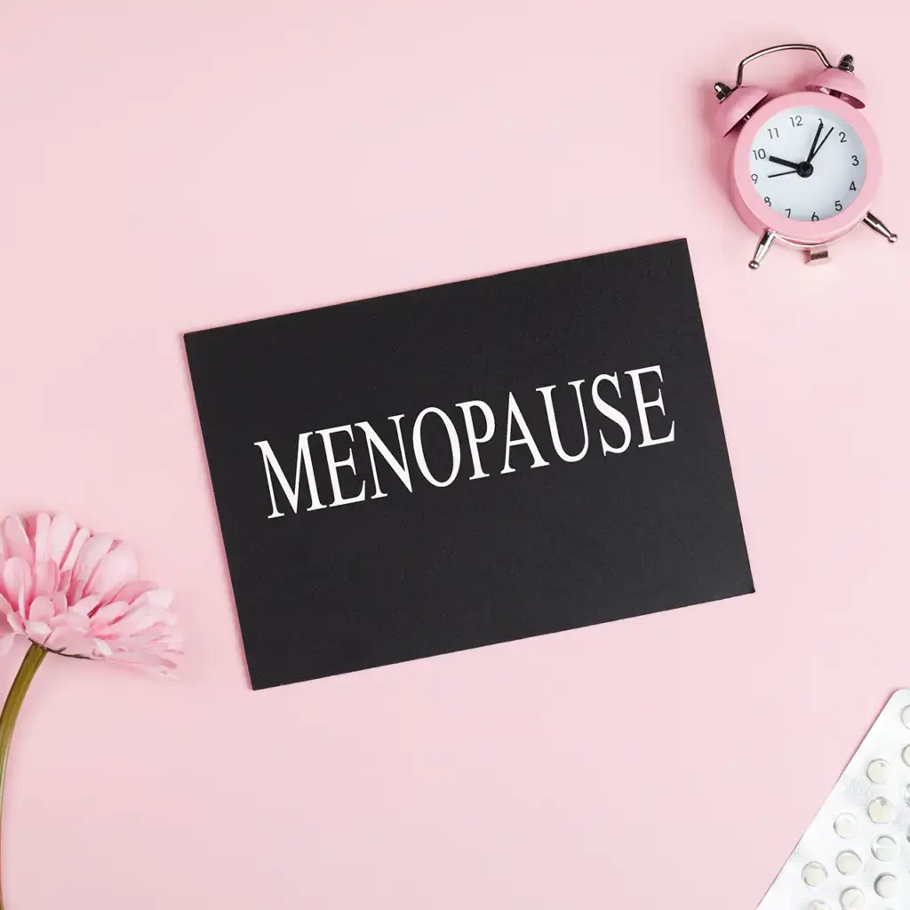 Menopause concept with clock, flower, and pills on pink.