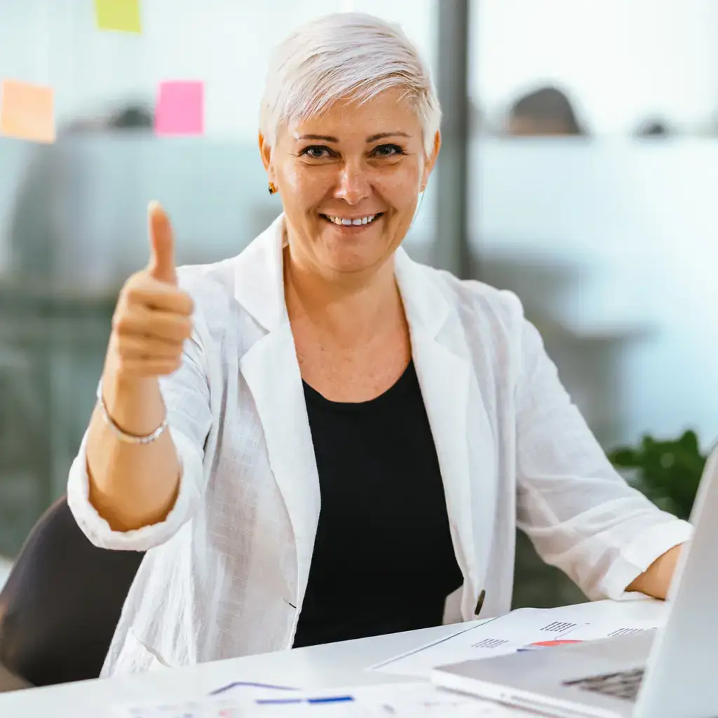 Happy businesswoman giving a thumbs-up gesture in an office.