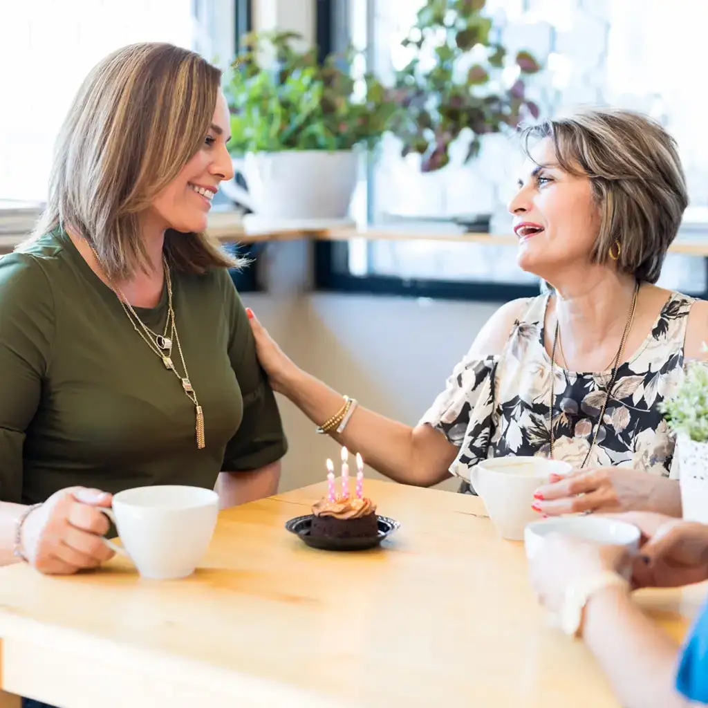 Two women celebrating a birthday with a cupcake in a café.