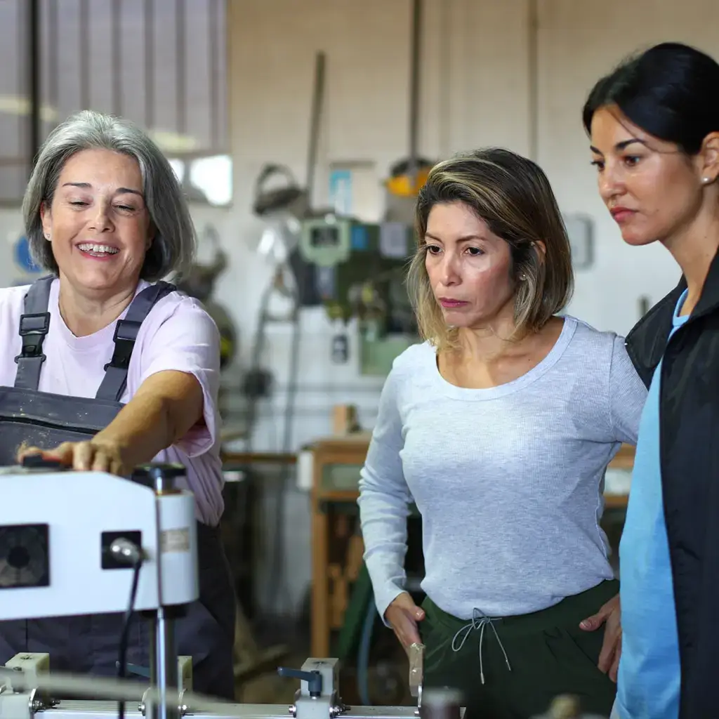 Three women learning to use machinery in a workshop.