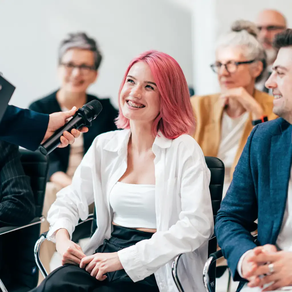 A young woman with pink hair smiling during an interview.